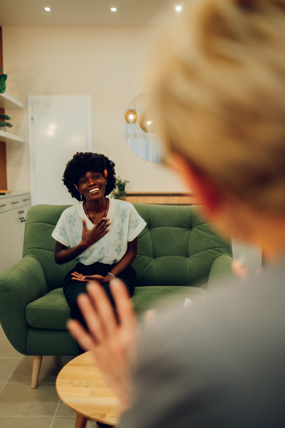 A happy woman is sitting with a psychotherapist in the office and smiling at her during her session.