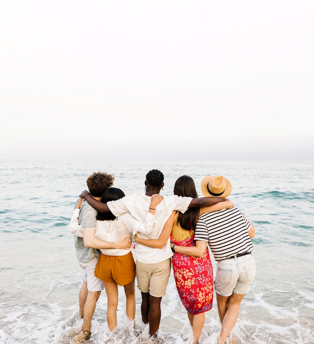 Rear view of young friends hugging each other during dual diagnosis treatment in front of the ocean.