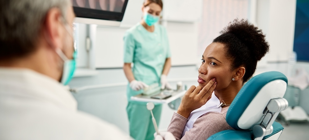 Woman talking to a dentist and complaining about pain in her teeth during dental checkup at dentist's office.