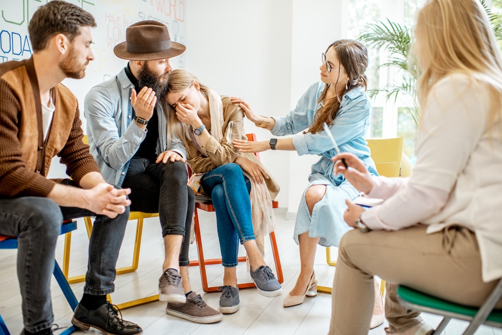 Young woman crying during the psychological therapy with group of people supporting her in outpatient addiction treatment program.